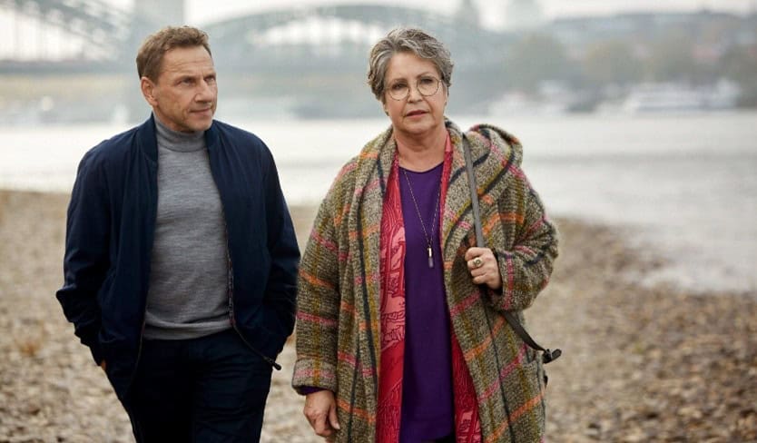 AltaText: Zwei erwachsene Personen beim Spaziergang am Fluss, entspannte Atmosphäre, naturverbunden, emotional.